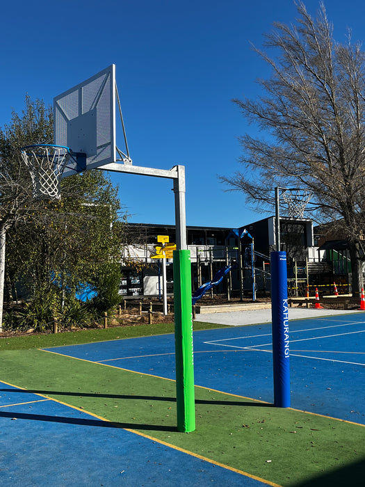 Basketball post, with post pad, on a playground with trees and buildings in the background