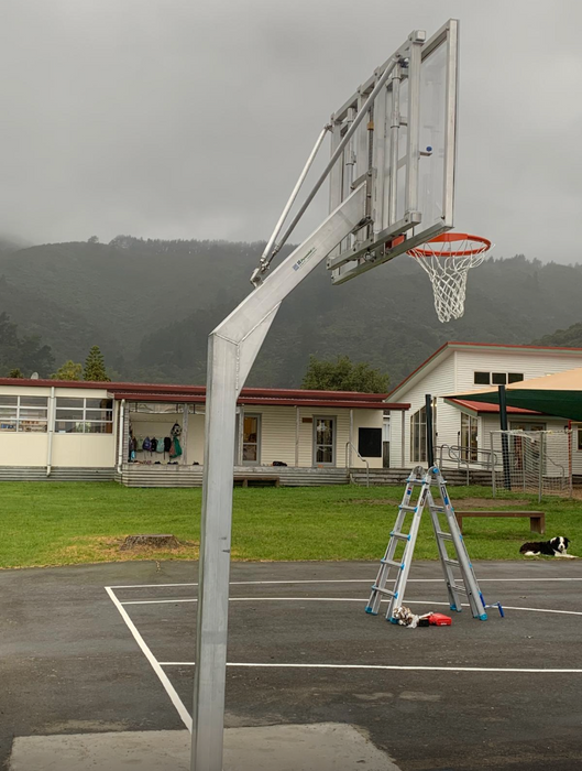 Basketball post and hoop tower with adjustable height from senior to junior, on an outdoor court with mountains in the background