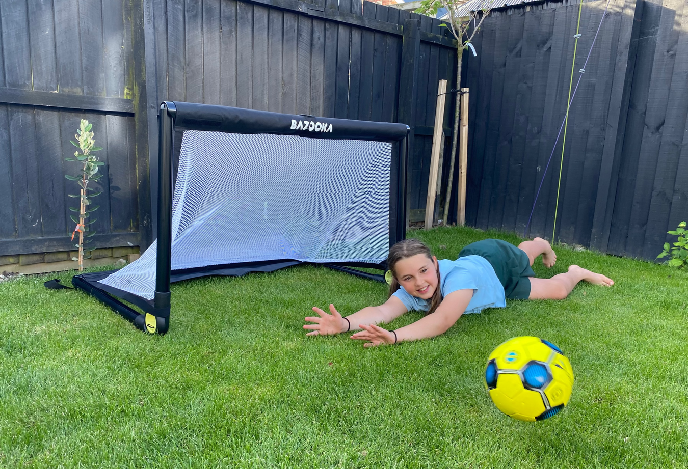 Child playing with a soccer ball next to a small goal in a backyard.