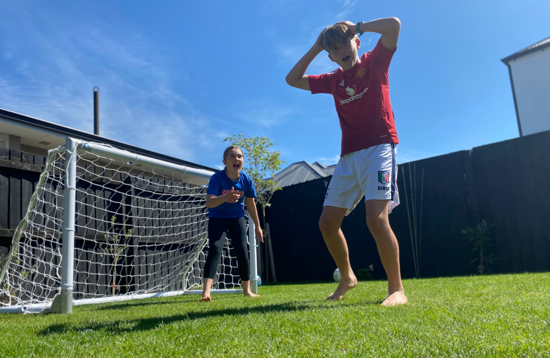 Two children playing soccer in a backyard with a clear blue sky.